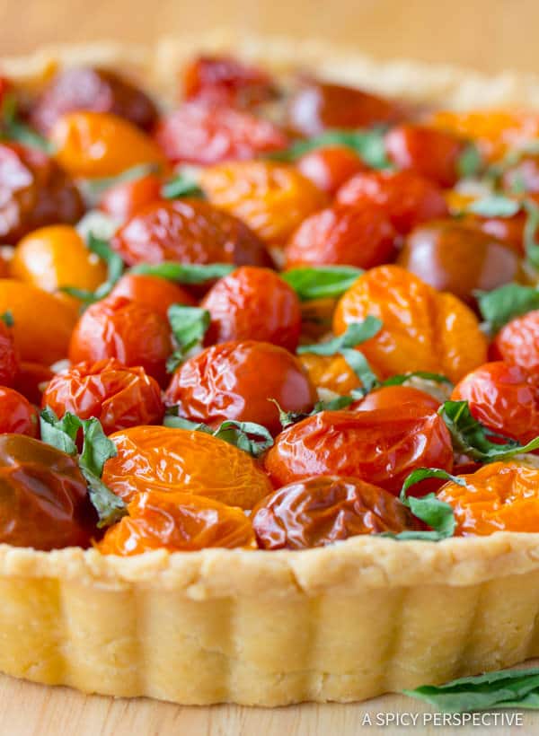 Side on view of a fresh cherry tomato tart with sliced basil scattered on top.