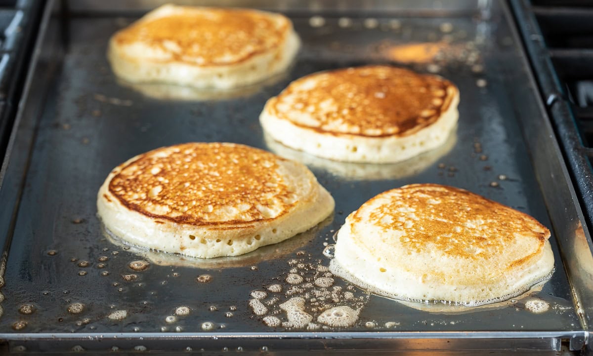 Golden brown pancakes being cooked on a griddle. 