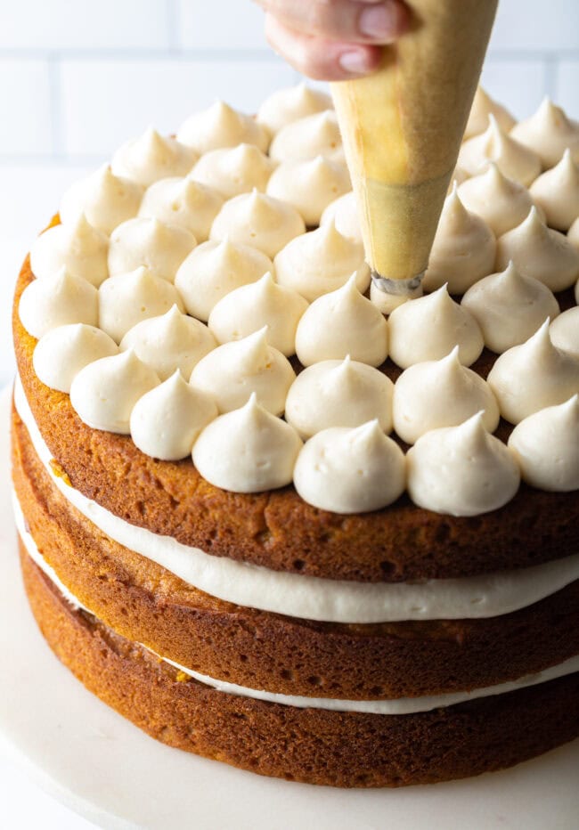 Hand piping frosting onto top layer of cake. 