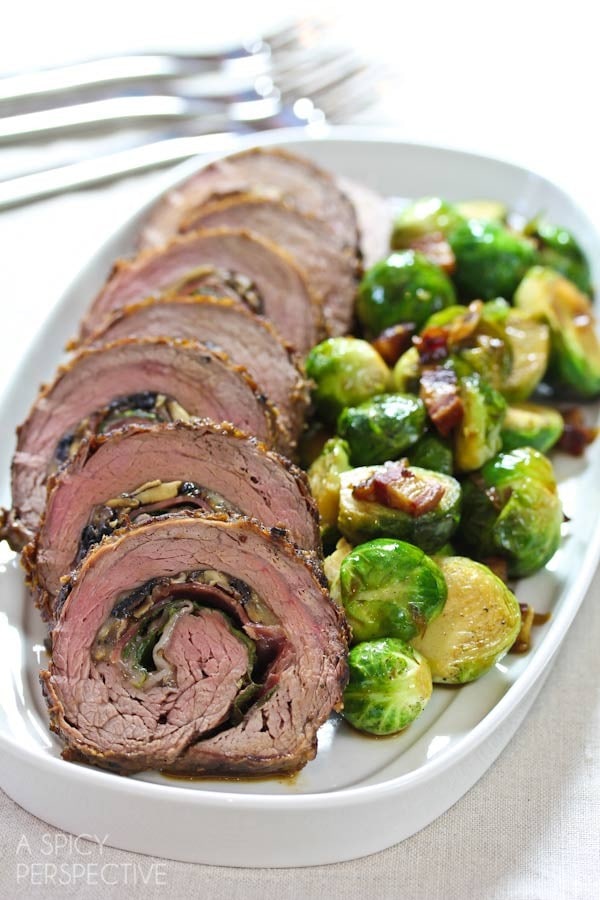 Stuffed flank steak wheels served on a platter with Brussel sprouts.