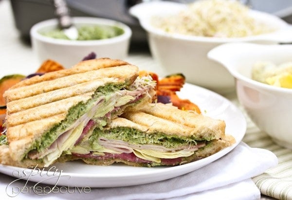 Halved panini Sandwich with Creamy Pesto Sauce on a white plate.