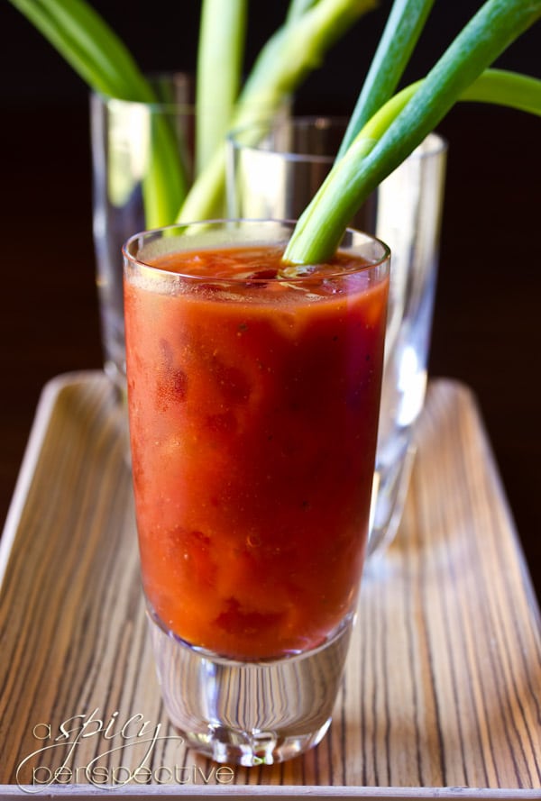 Side view of a bloody mary with a garnish of fresh scallion. 