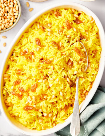 Saffron Rice with Golden Raisins and Pine Nuts on a plate with more in a bowl in the background.