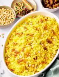 White oval dish filled with yellow saffron rice and raisins with pine nuts.