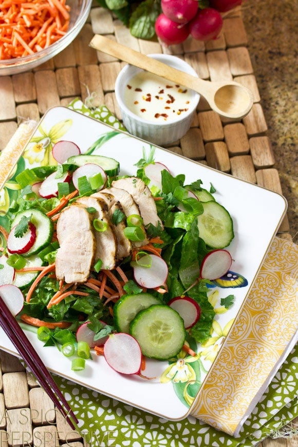 White square plate of Banh Mi Salad with fresh salad greens, sliced cucumbers and radishes, shredded carrots, and slices of grilled chicken breast.