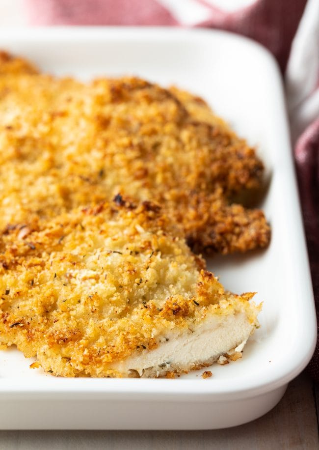 Baked chicken cutlet on a white plater with a slice removed. 