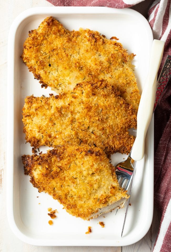 Plated cooked chicken cutlet with a fork and bite taken out. 