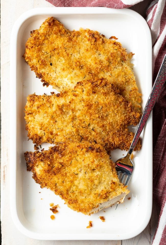 Overhead view of three pieces of baked chicken cutlets on a platter. 