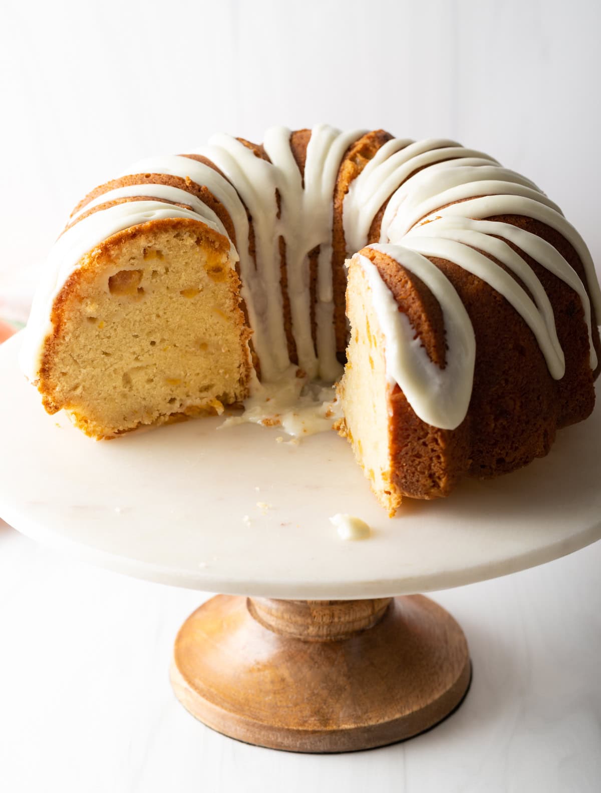 Peach bundt cake on a stand that has a few pieces removed.