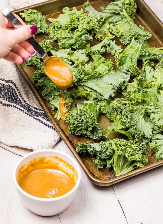 Hand pouring butter spice mixture over kale chips. 