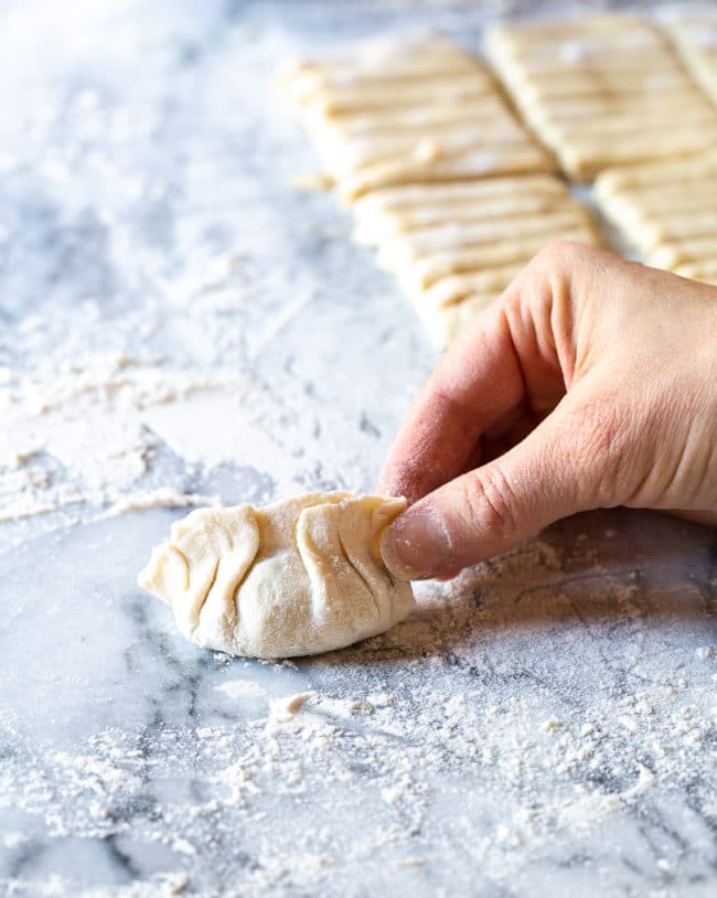 Hand pinching together dumpling with detailed folds. 
