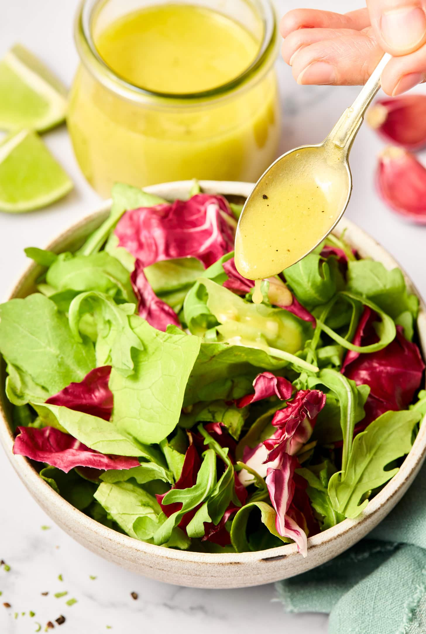 A spoonful of lime vinaigrette is being poured over a fresh greens salad.