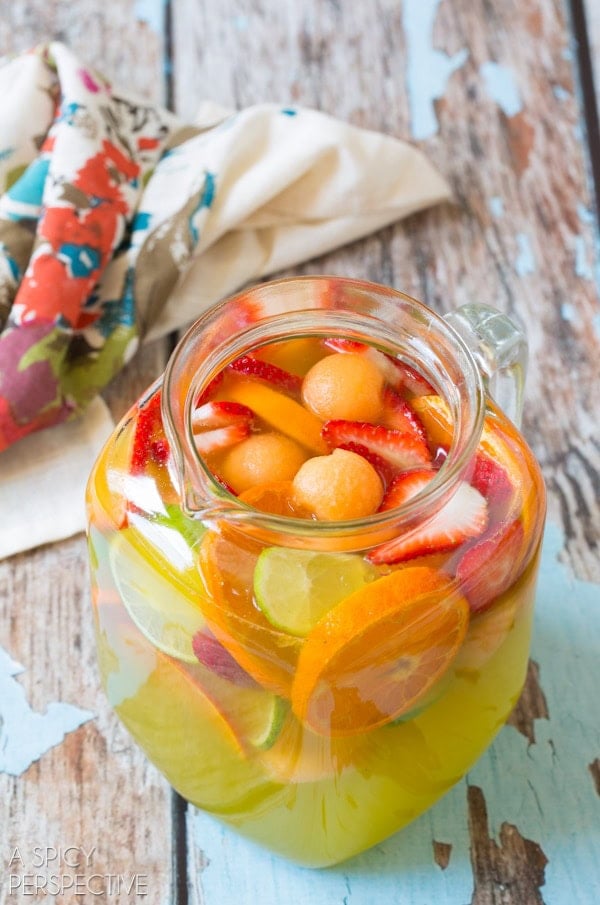 Glass pitcher filled with white sangria and cut up fruit.