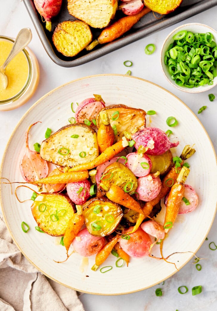 Roasted root vegetables on a sheet pan with a spatula. 