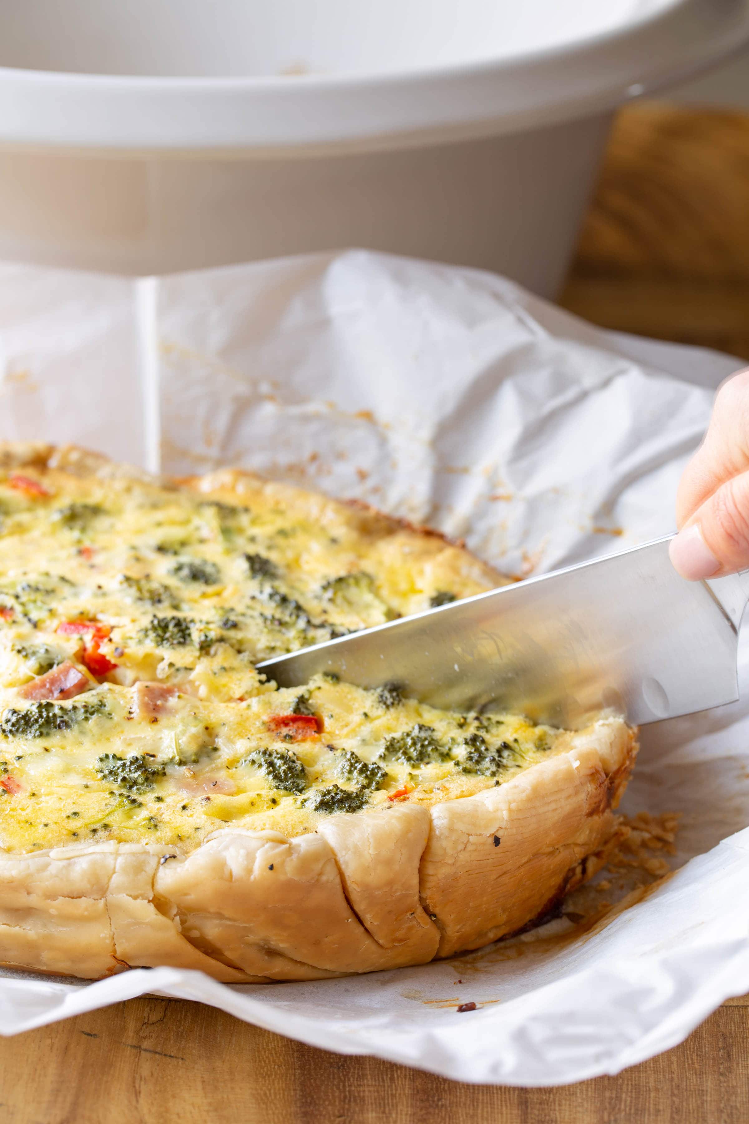 A sharp knife cutting breakfast quiche that's on a piece of parchment paper.