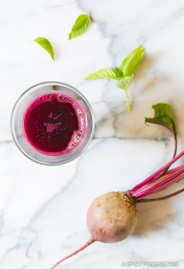 Top down view of basil juice in a glass with a beet laid out on a countertop. 