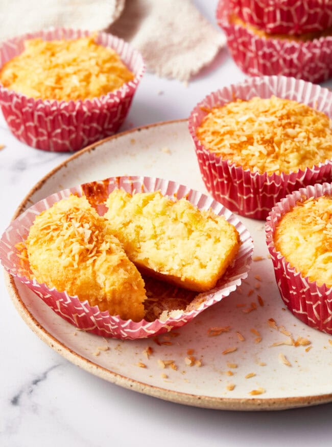 A tropical breakfast muffin split in two on a white plate. More muffins are in the background.