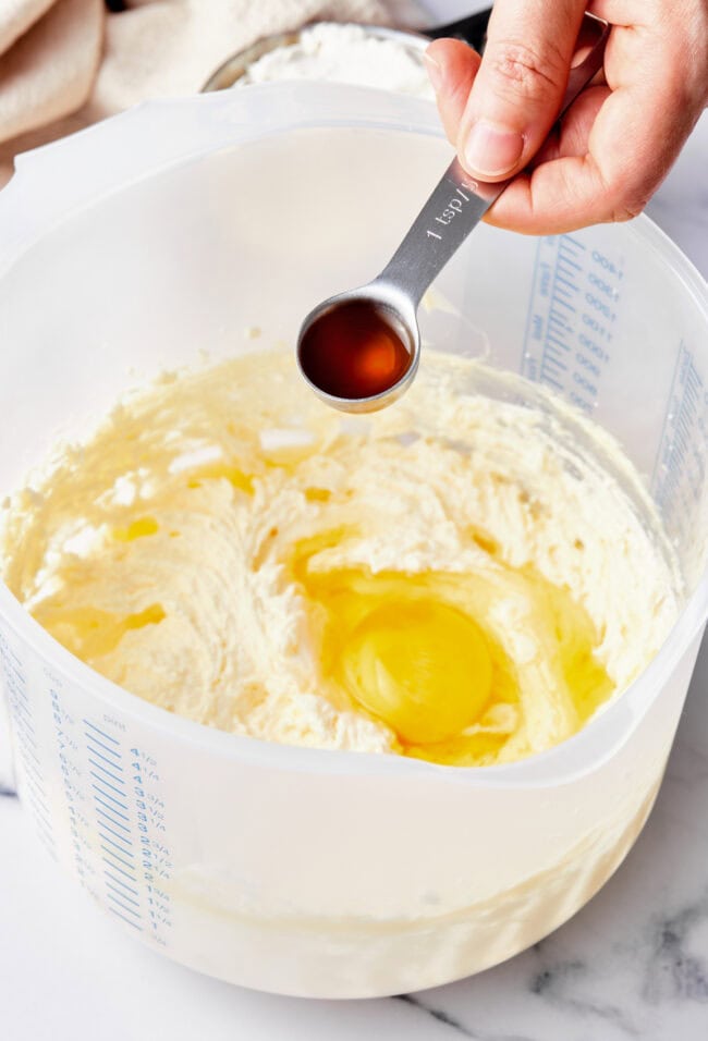 A hand adding vanilla to a mixing bowl with muffin batter.