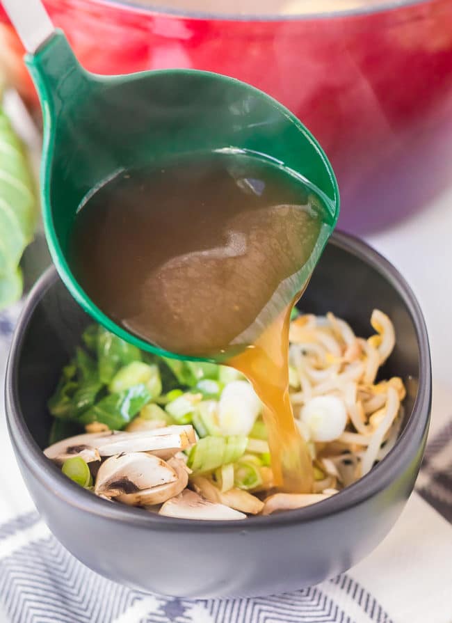 Ladle pouring broth over veggies in a bowl.