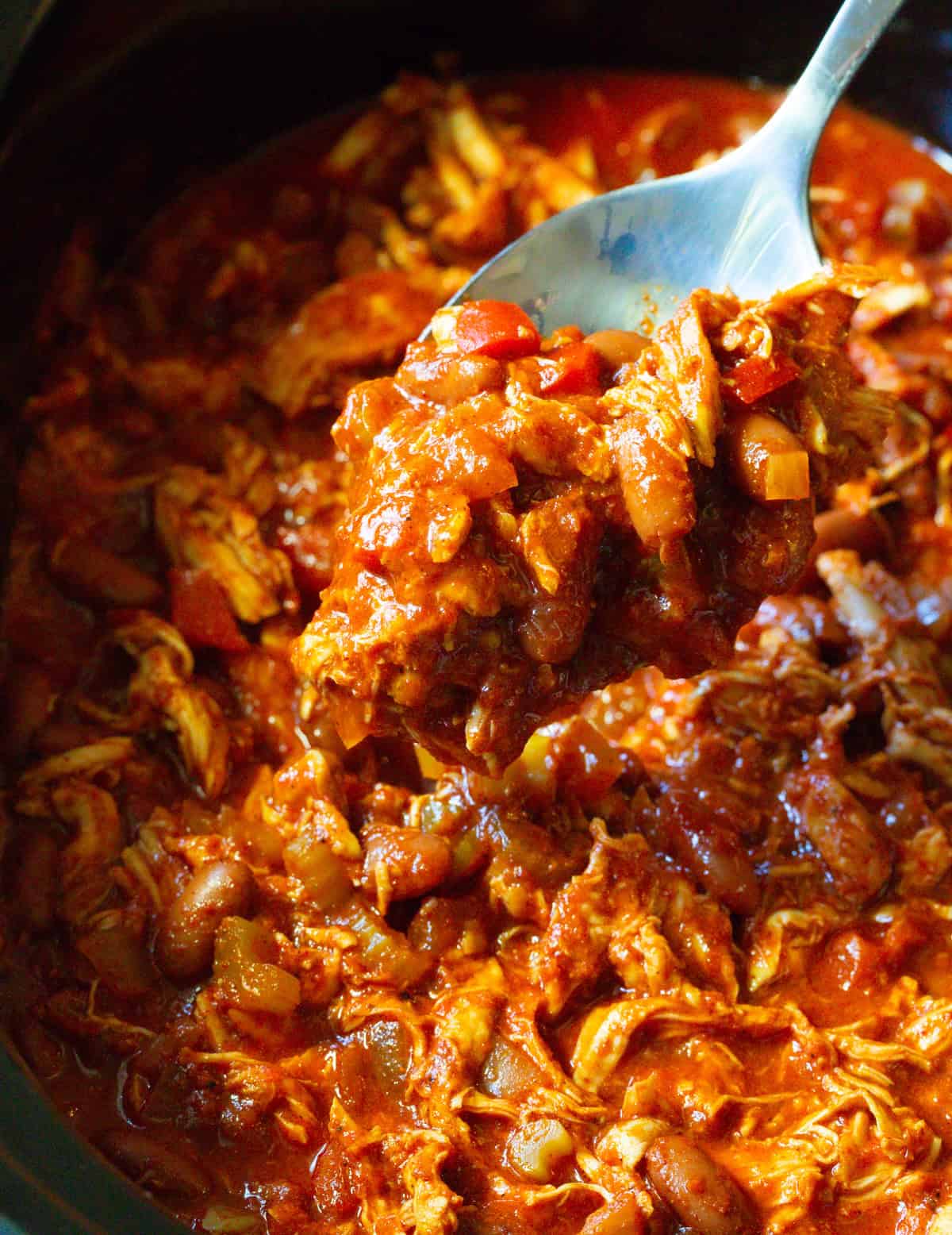 red pepper chicken chili recipe in crock pot with spoon lifting it up