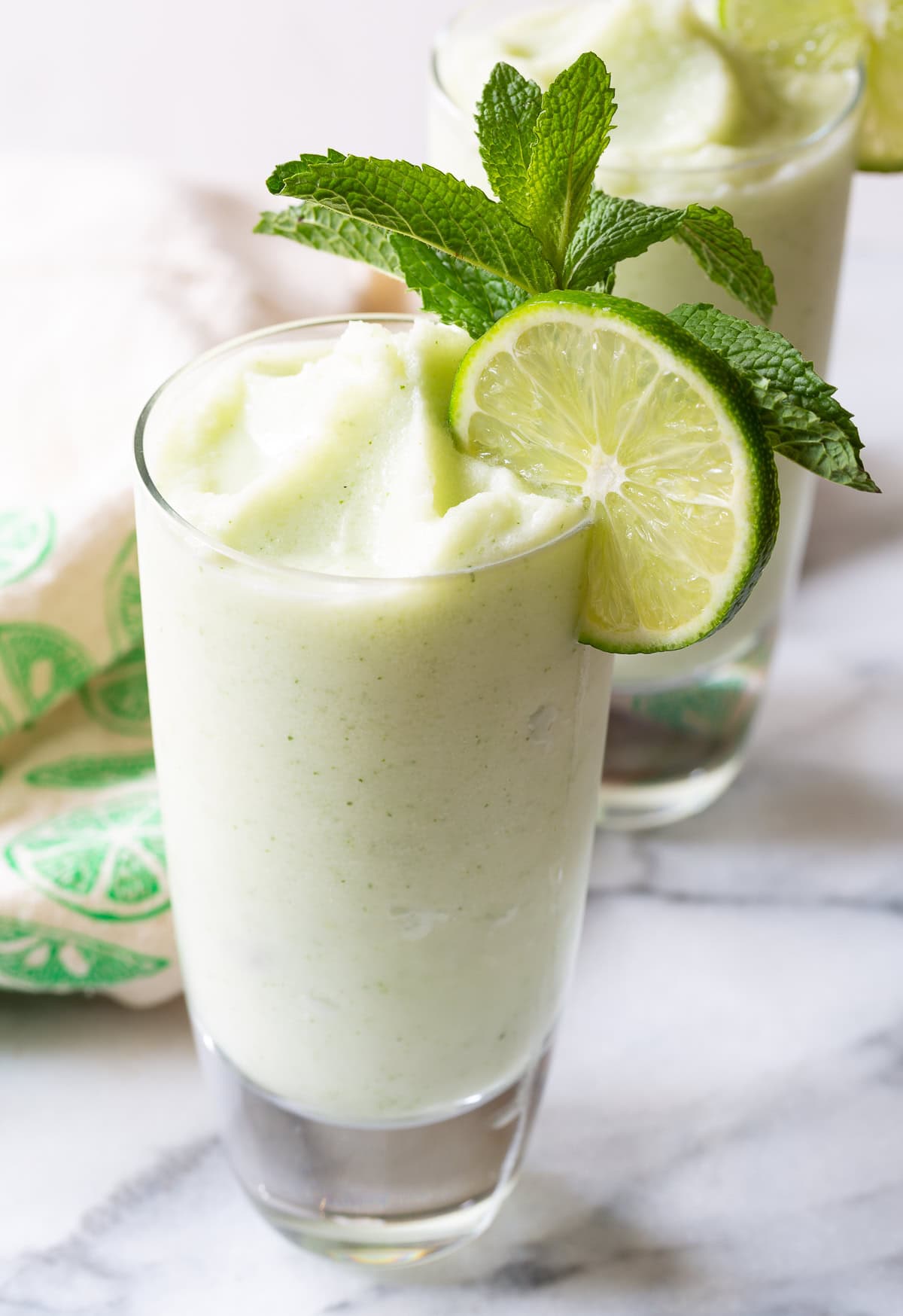 Glass of frozen mojito cocktail garnished with a lime wheel and fresh mint sprig.