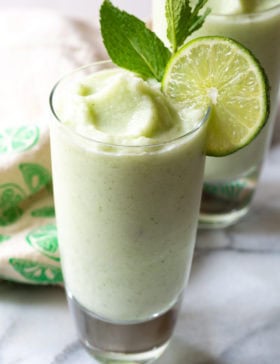 Side-on close up of a froze coconut mojito with a lime wheel and mint sprig.