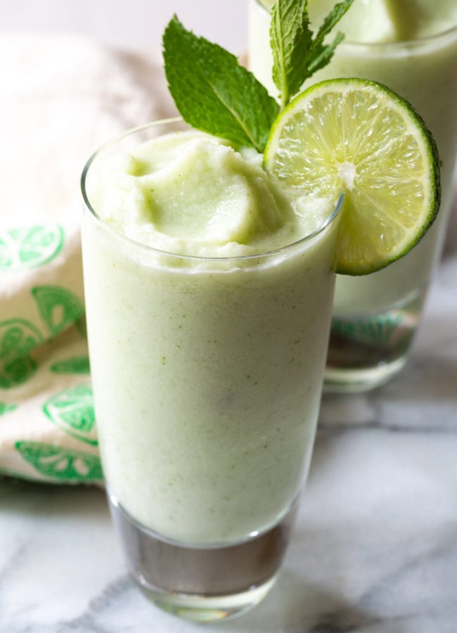 Side-on close up of a froze coconut mojito with a lime wheel and mint sprig.