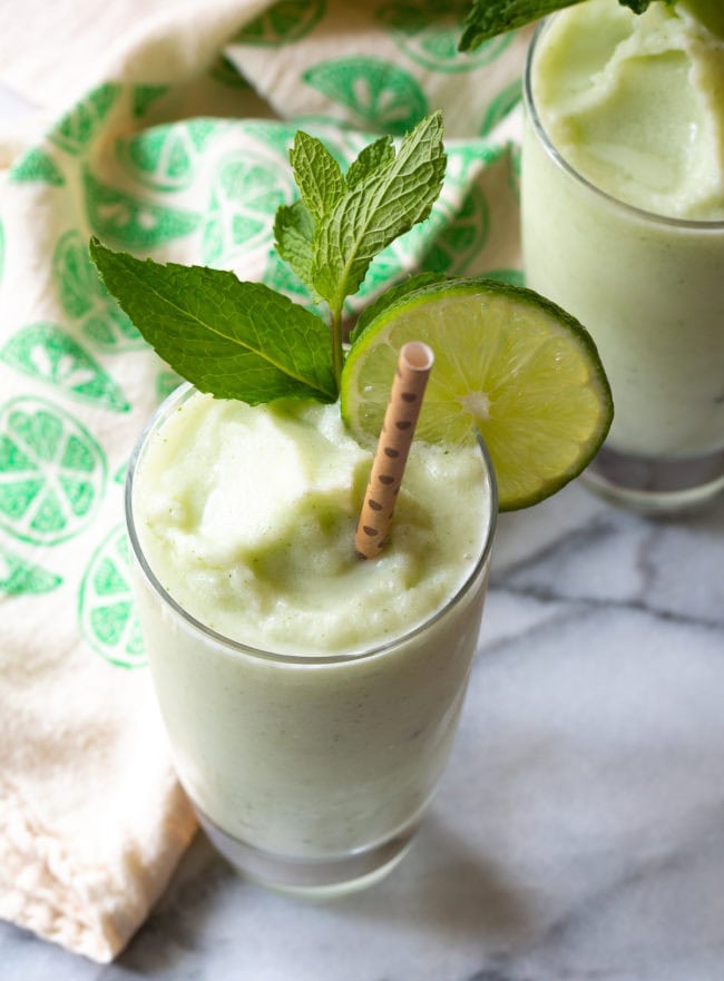 Frozen coconut mojito in a tall glass with a lime wheel, mint sprig and a striped gold straw.