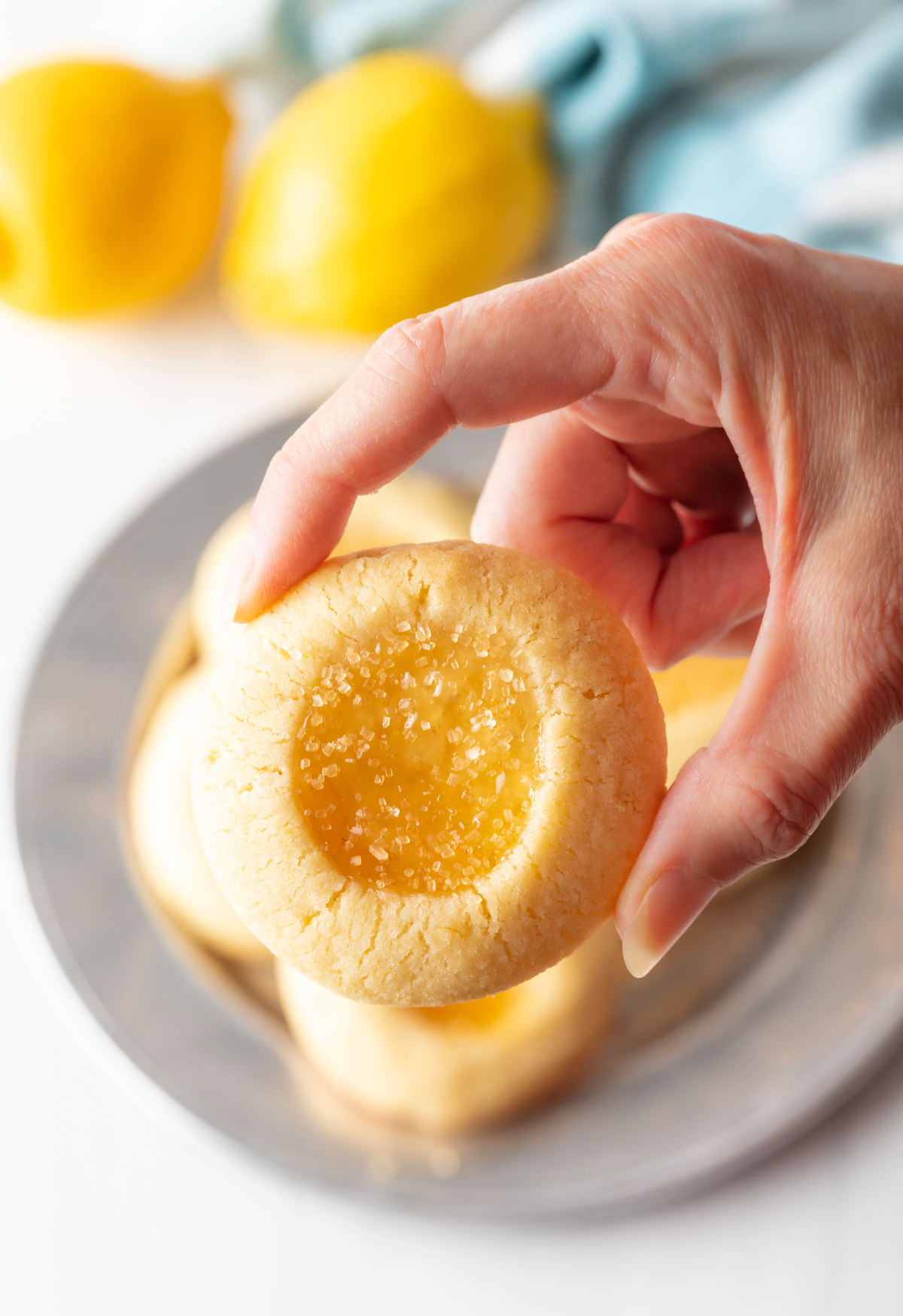 Hand holding up a lemon drop cookie for the camera for you to get a good up close look at the 
