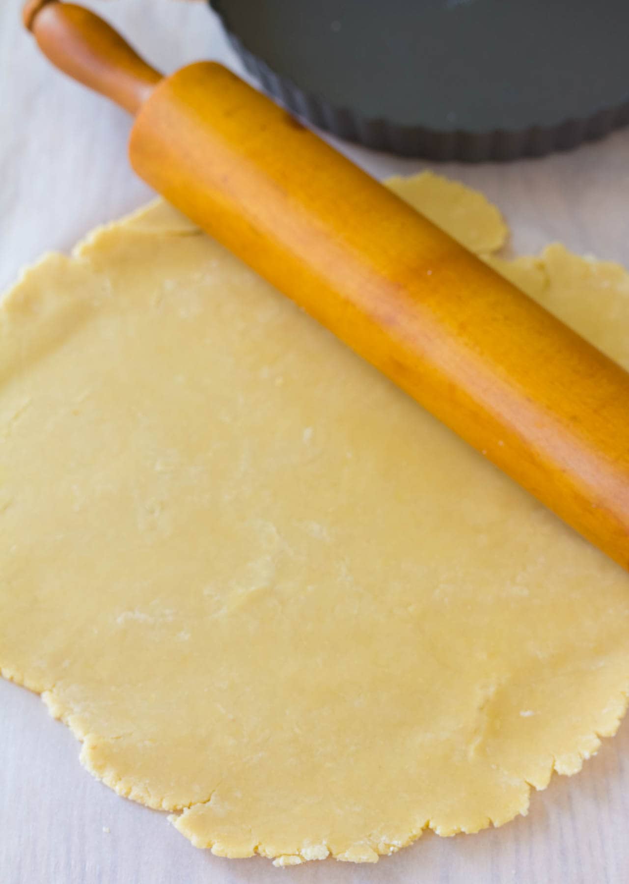 Rolled out pie crust with the tin in the background and a rolling pin resting on one side of the crust.