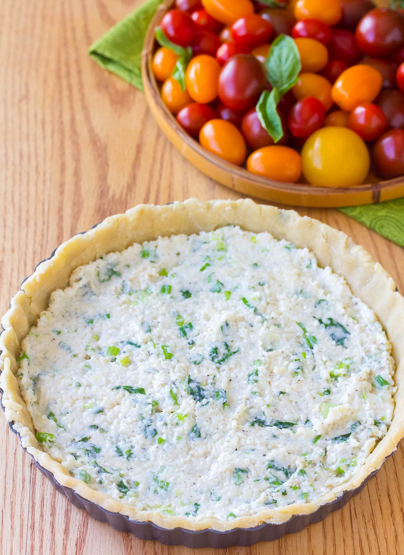 Creamy herb filling spread over the bottom of a pie crust. A bowl of cherry tomatoes is sitting in the background.
