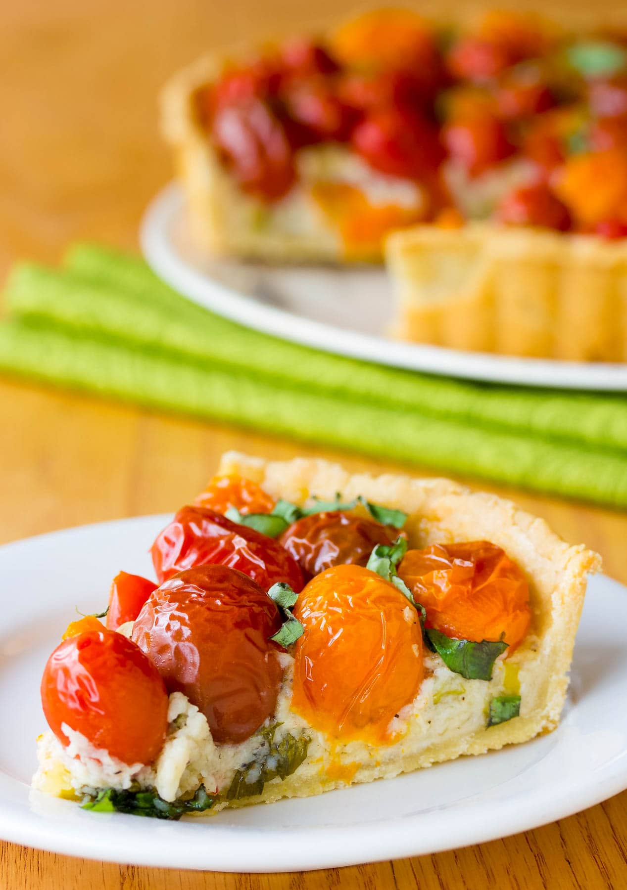 Slice of cherry tomato tart on a white plate. The rest of the tart is in the background.