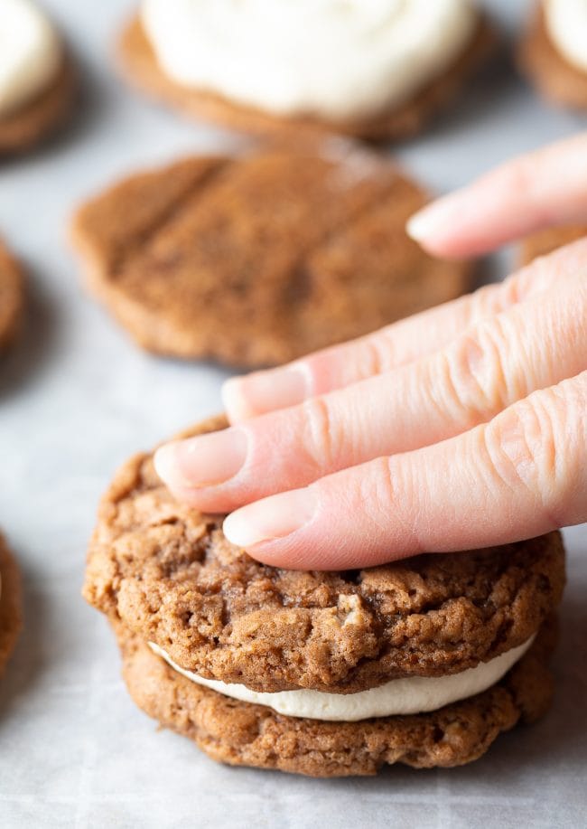 Hand pressing top layer of oatmeal cookie over cream filling. 