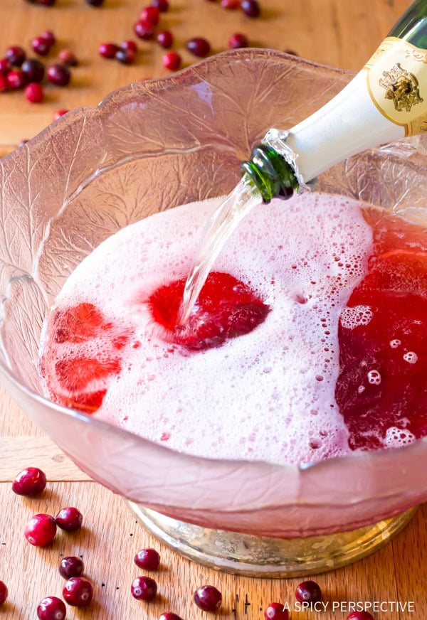 Christmas Champagne Punch ingredients added to a punch bowl with cranberries in the background