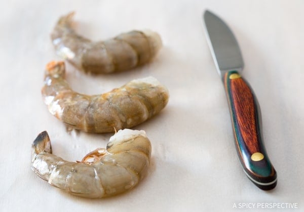 Raw shrimp on a baking sheet next to a paring kinfe.