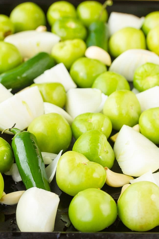 Tomatillos, peppers, onions and garlic on a baking tray before roasting.