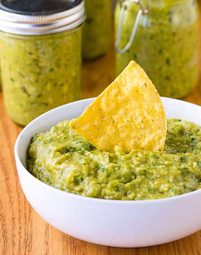 White bowl of tomatillo avocado salsa verde with a chip sticking out of the dip.