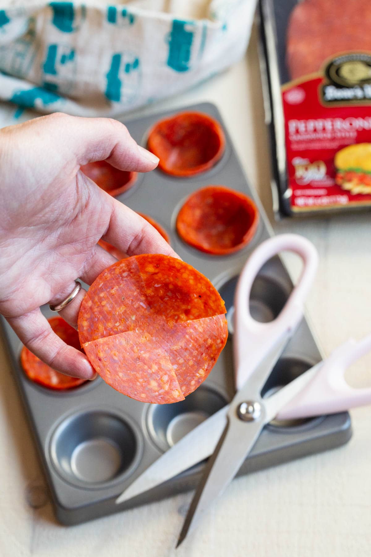 Hand holding up a slice of pepperoni which has been cut by a scissor. 