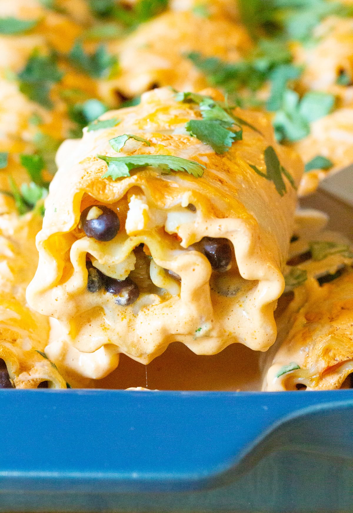 Spatula taking a lasagna roll up from a blue baking dish. 