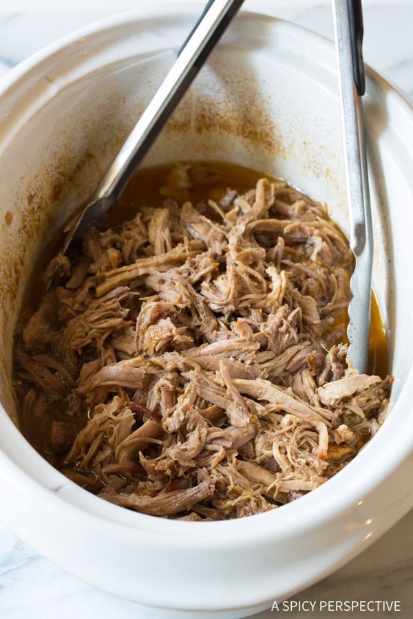 Shredded pork in the crockpot with metal tongs.