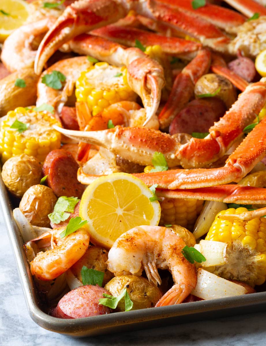 baked seafood boil that you broil in the oven. A large sheet pan is loaded with cooked shrimp, pieces of corn, whole baby potatoes, slices of sausage, and crab legs.