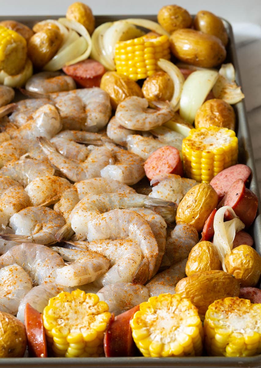 Raw seasoned shrimp, sausage, and corn with roasted potatoes all on a baking sheet to broil.