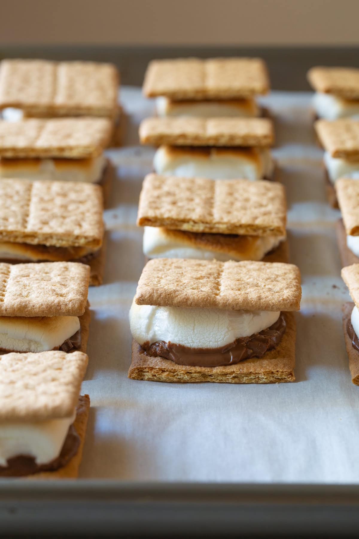 How To Make Smores In The Oven - Baked s'mores lined up on a baking sheet.