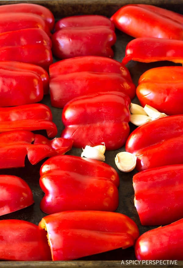 Red peppers and garlic cloves on a baking sheet. 