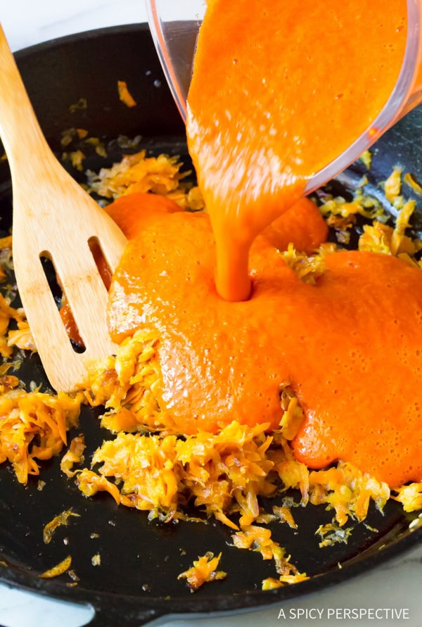 Pouring the blended red peppers into a pan with carrots and onions. 