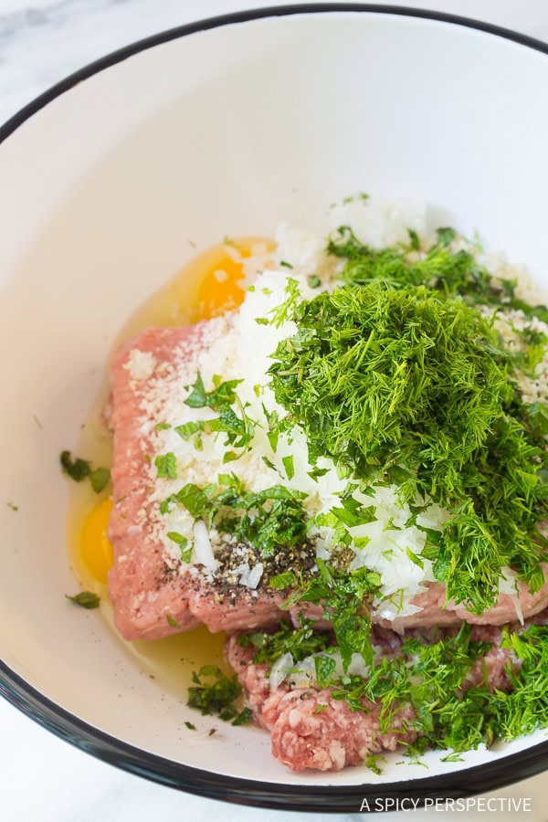 Ground meat will all ingredients needed to make Greek meatballs in a mixing bowl. 