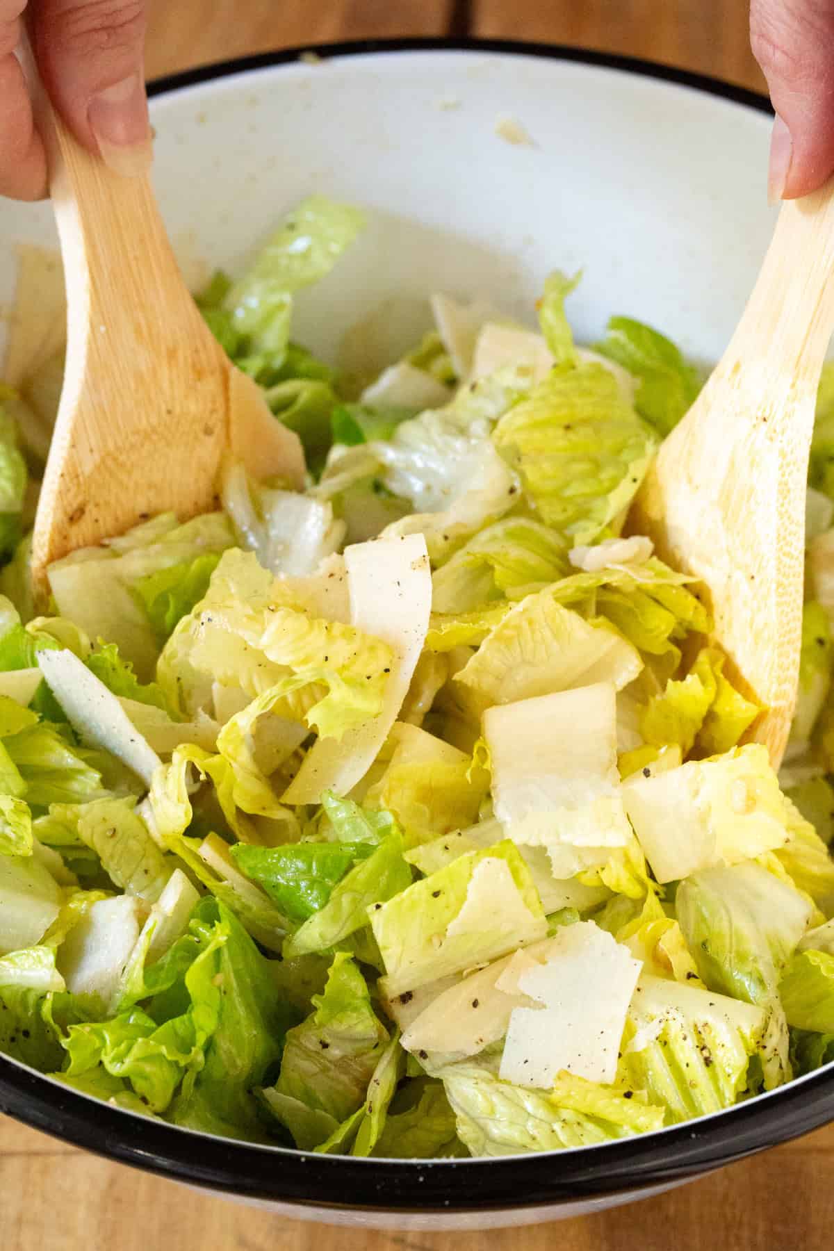 Hands mixing together steakhouse salad with tongs. 