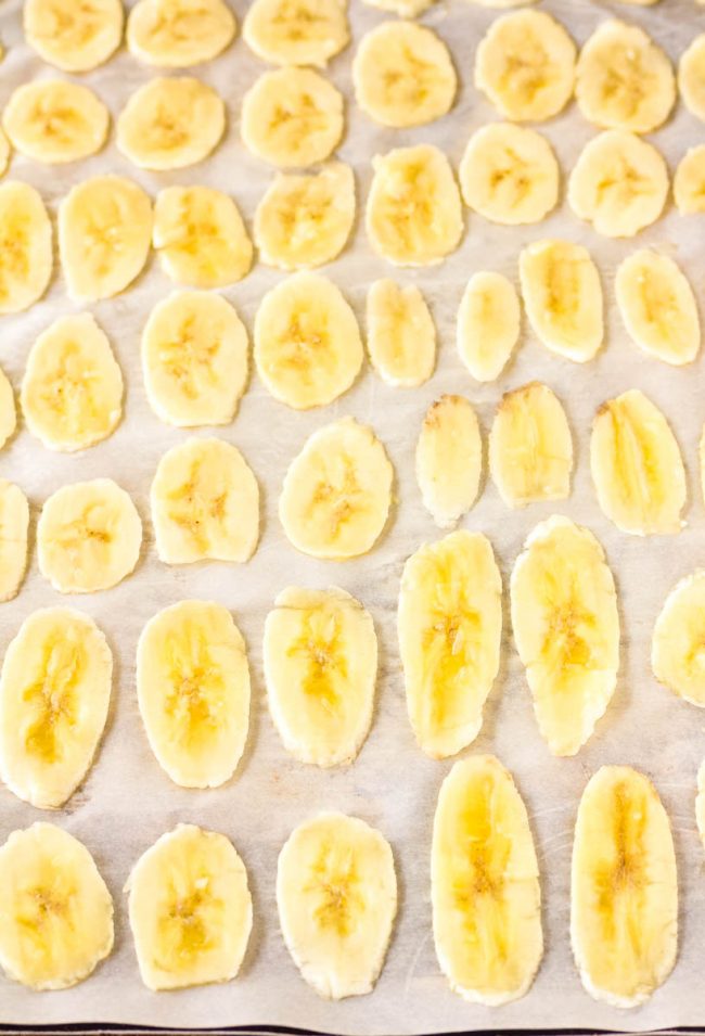 Laying these banana chips out on a cookie sheet to bake in the oven 
