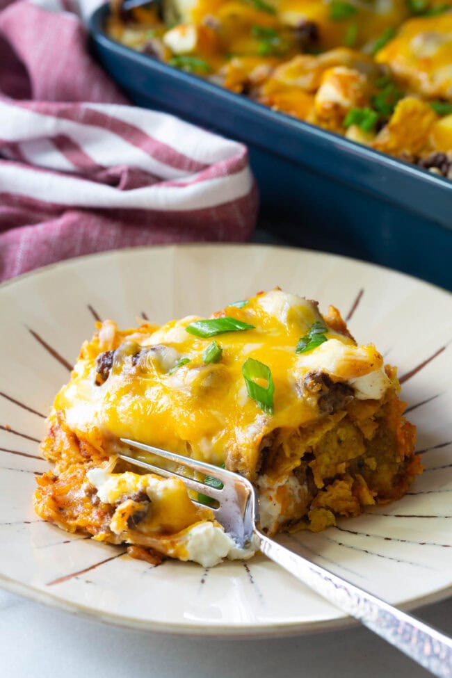 A piece of Doritos casserole on a plate with a bite taken out by a fork.