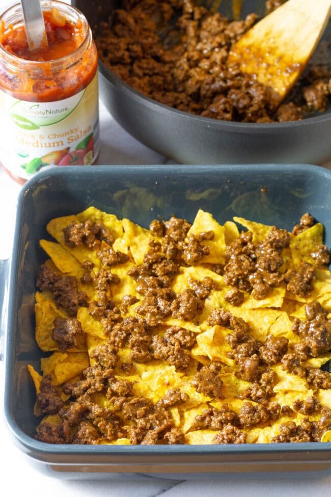 Doritos covered with cooked minced meat in baking dish.